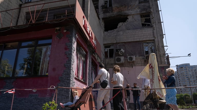 People look at an apartment building damaged by a drone...