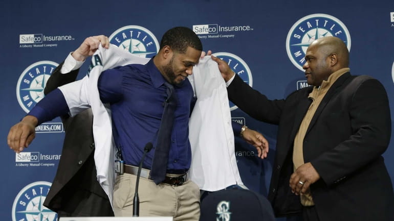 Robinson Cano, center, is helped into his new jersey by...