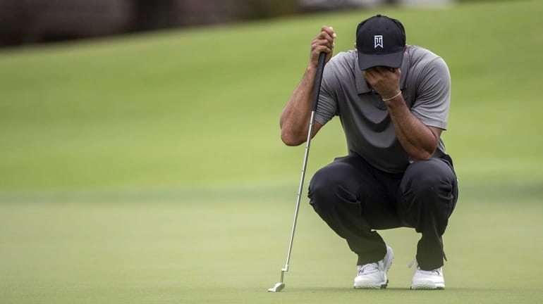 Tiger Woods covers his face as he waits to putt...