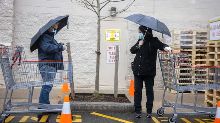 Shoppers dodge the rain while practicing social distancing on line outside...