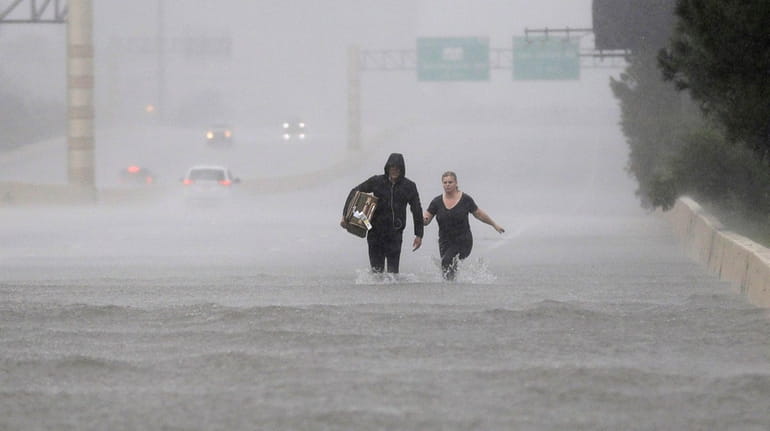 Two people walk down a flooded section of Interstate 610...