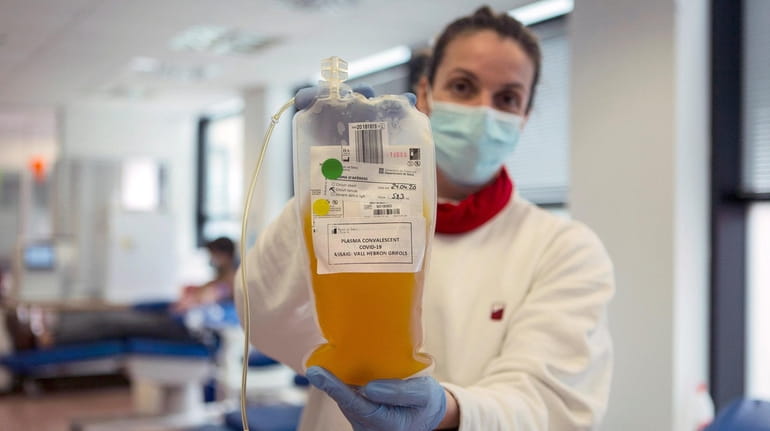 A nurse holds up a bag of plasma donated by...