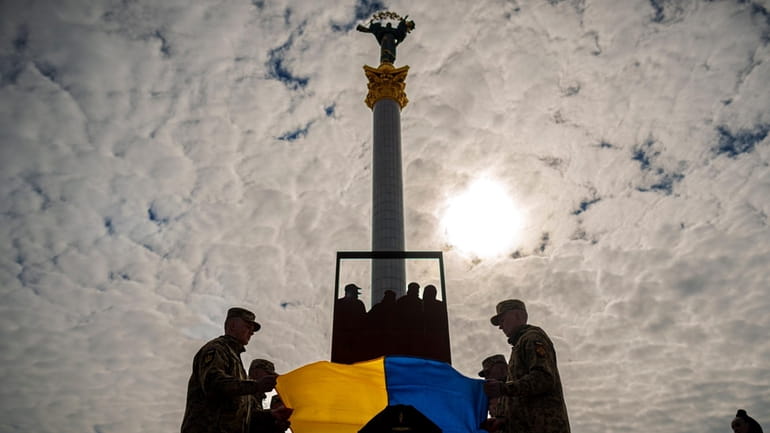 Ukrainian servicemen place the national flag on the coffin of...