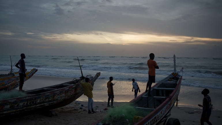 Senegalese youth gather around pirogues on the beach at dusk...