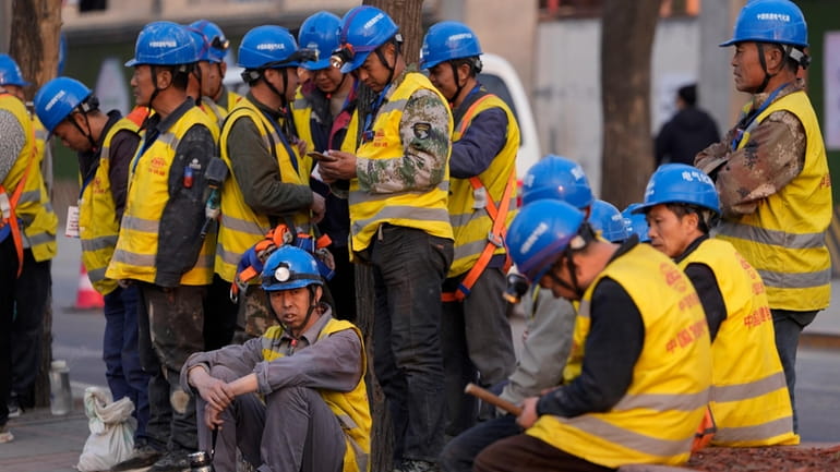 Workers wait for transport outside a construction site in Beijing,...
