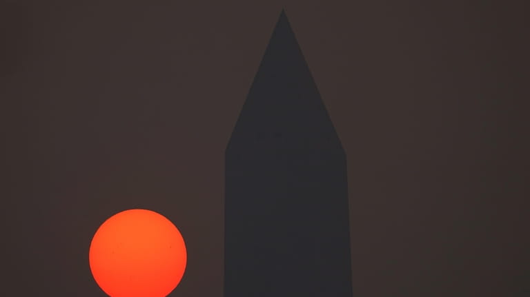 The sun rises behind the Washington Monument and a thick...