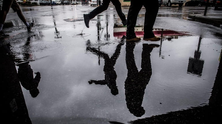 Pedestrians make their way through puddled streets in Wantagh, Friday...