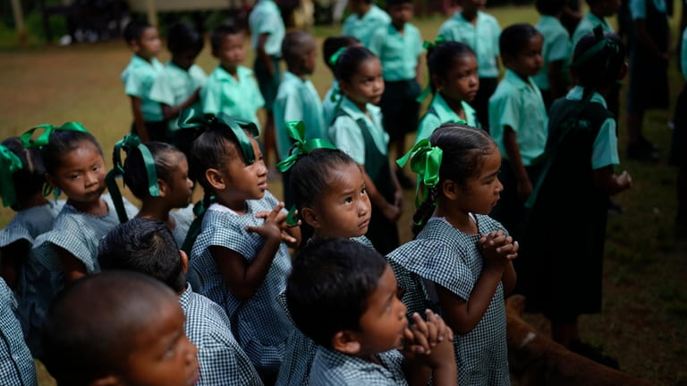 Amerindian children line up to sing their country's national anthem,...