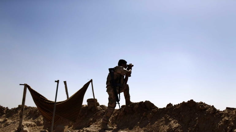 A Kurdish Peshmerga fighter uses binoculars to check on Islamic...