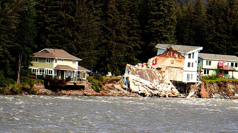 A home hangs over the edge of an eroded riverbank...