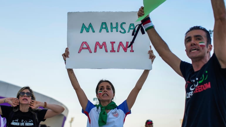 A woman holds up a sign reading Mahsa Amini, a...
