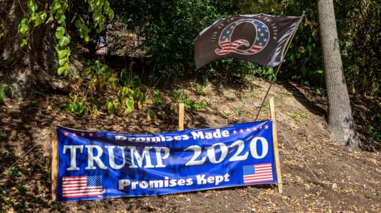 A Trump 2020 sign and a QAnon flag are displayed...