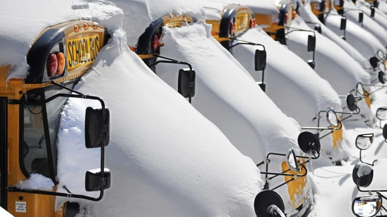 School buses are covered in snow after a winter storm...