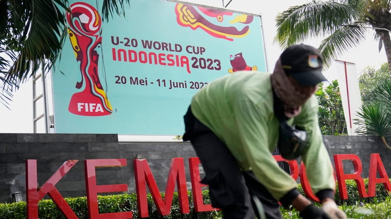 A worker trims grass near a banner of FIFA U-20...