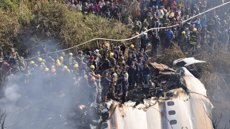 Nepalese rescue workers and civilians gather Sunday around the wreckage of...