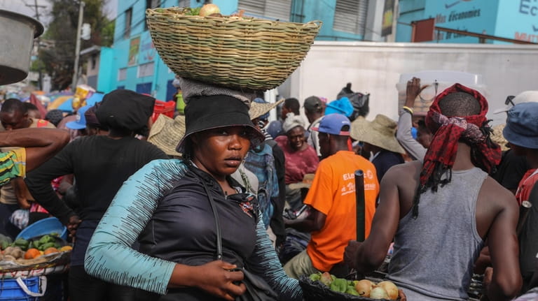 A street vendor balances a basket of vegetables on her...
