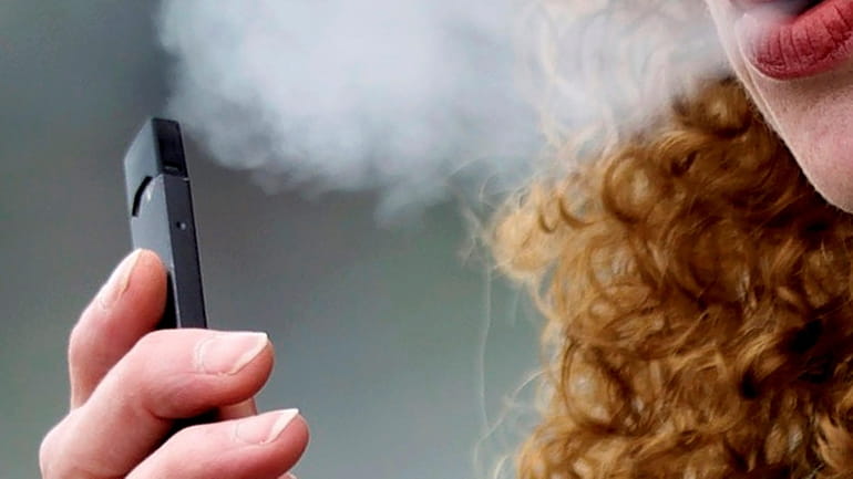 A woman exhales while vaping from a Juul pen e-cigarette...