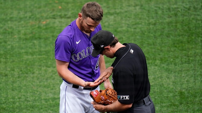 Umpire Alex MacKay, right, examines the hand and glove of...