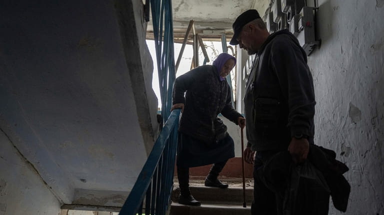 A volunteer helps Olga, 79, walk down the stairs from...