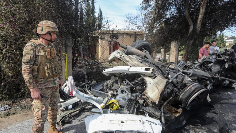 A Lebanese army officer stands next to a destroyed car...