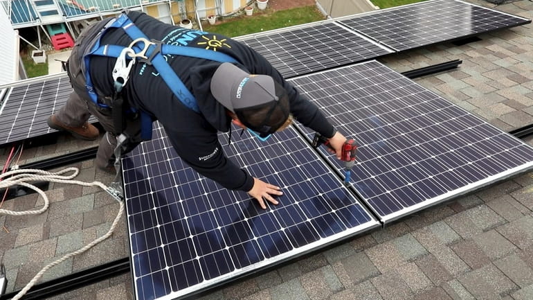 A worker intalls solar panels on the roof of a...