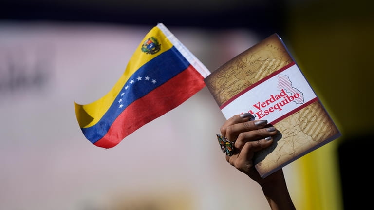 A woman holds a Venezuelan flag and a book about...