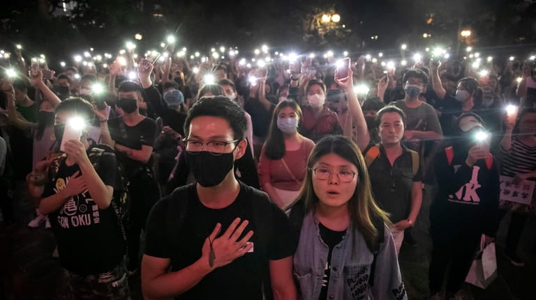 Demonstrators hold their cellphones aloft as they sing "Glory to...