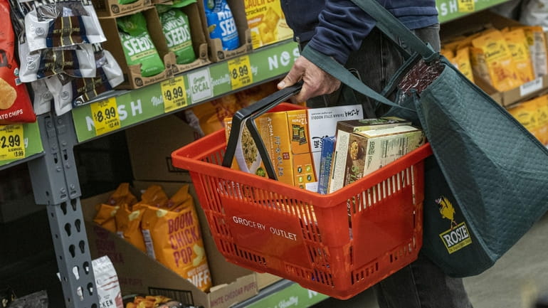 A shopper holds a shopping basket with groceries inside a...