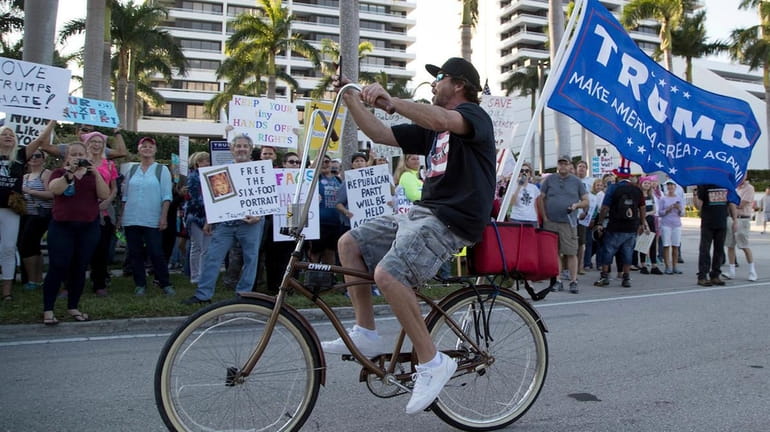 Dylan Moye rides his bike past Donald Trump protesters gathered...