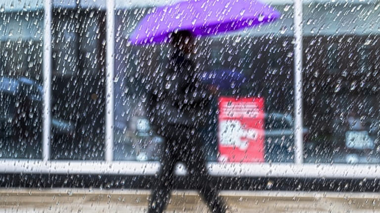Raindrops fall on a window pane as a pedestrian walks...