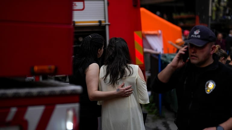 Two women gather as firefighters and emergency teams work in...