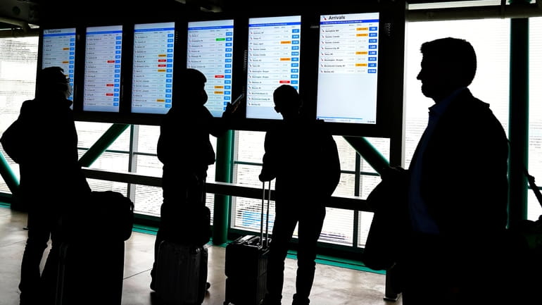 Travelers check American Airlines flight information screens for their flight...