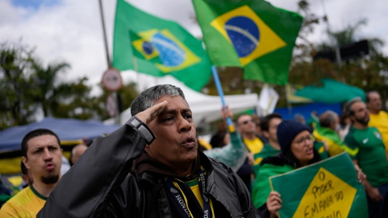A supporter of Brazilian President Jair Bolsonaro salutes while singing...