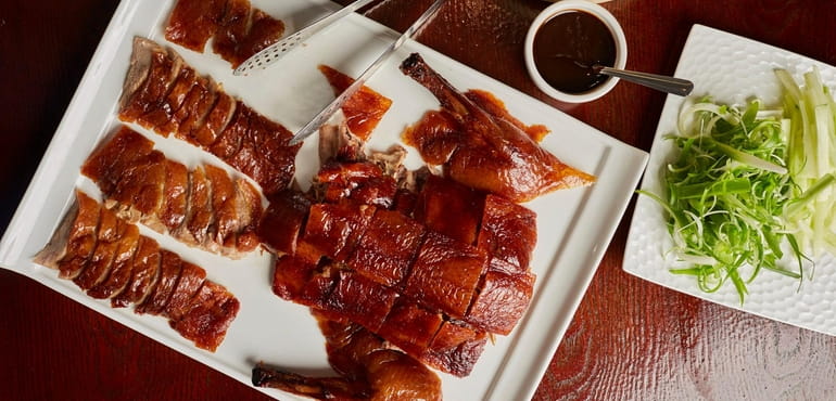Peking duck is masterfully carved and served with buns, slivered scallions,...