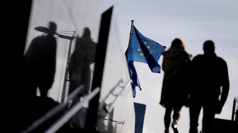 A couple walk past EU flags outside EU headquarters in...