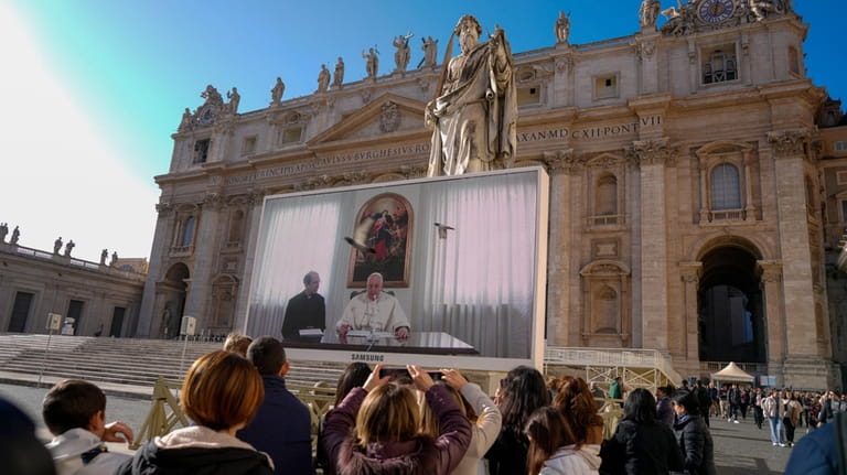 Pope Francis appears on a giant monitor set up in...
