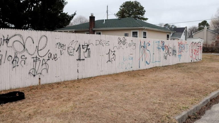 MS-13 gang and other graffiti is painted a fence on...