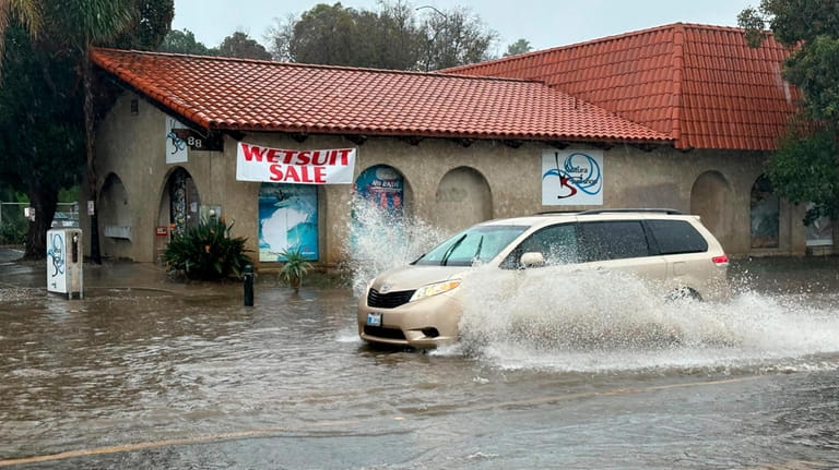 A vehicle drives through water on a flooded street in...