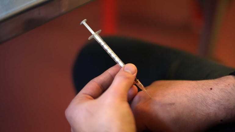A heroin addict injects a heroin shot in a room,...