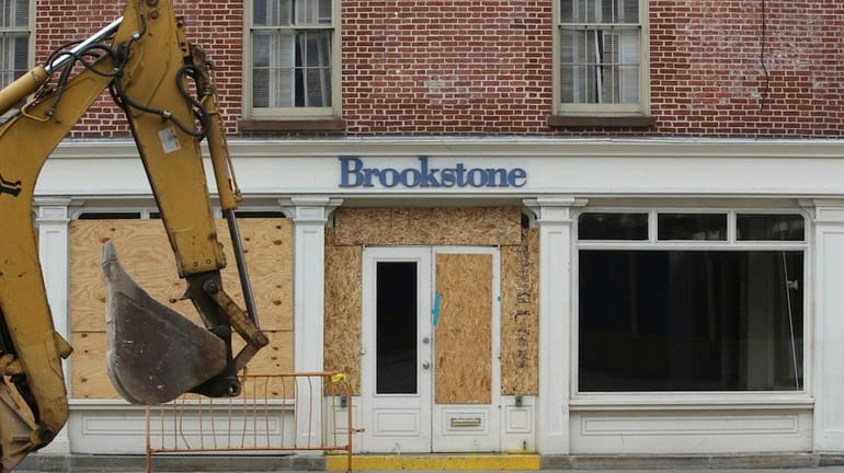 A backhoe is driven past the shuttered Brookstone store on...