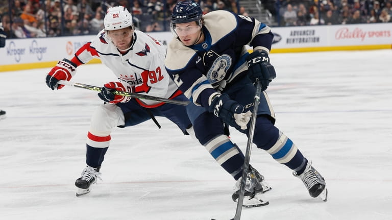 Columbus Blue Jackets' Andrew Peeke, right, carries the puck past...