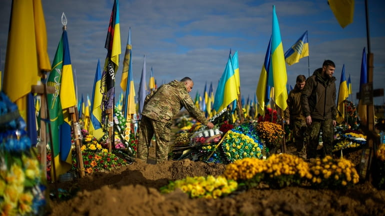 A Ukrainian serviceman places flowers on the grave of a...