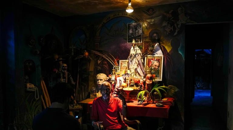 Juan Gonzalez sits next to his altar adorned with religious...