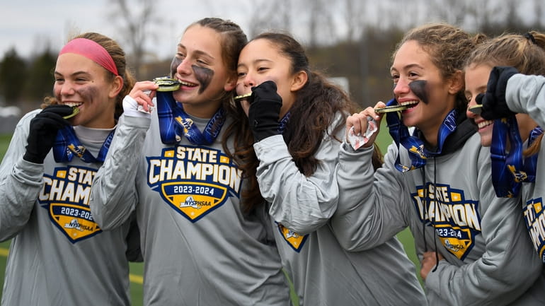 Ward Melville girls soccer players bite their medals after winning...