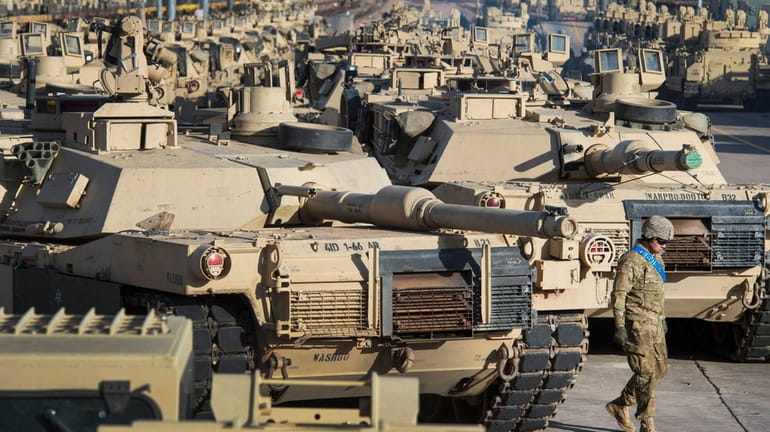 A soldier walks past a line of M1 Abrams tanks,...