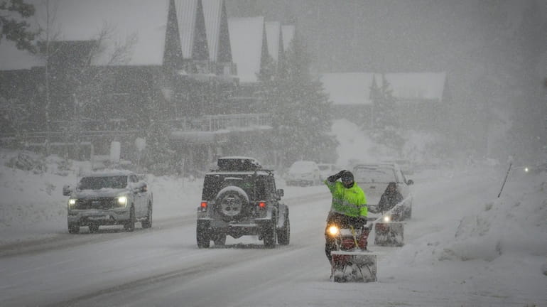 Workers attempt to clear a road with snow blowers during...