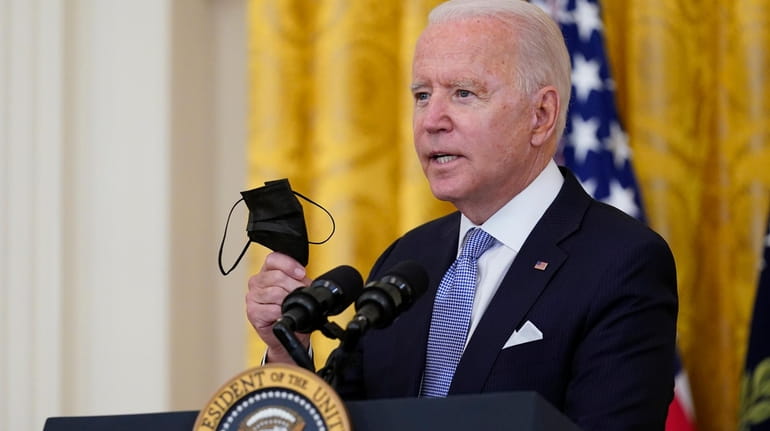 President Joe Biden holds a face mask as he announces...