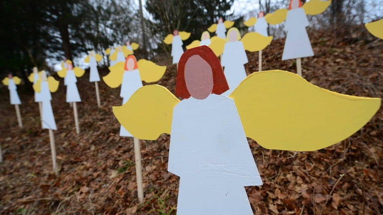 Twenty-seven angel wood cutouts are set up on a hillside...