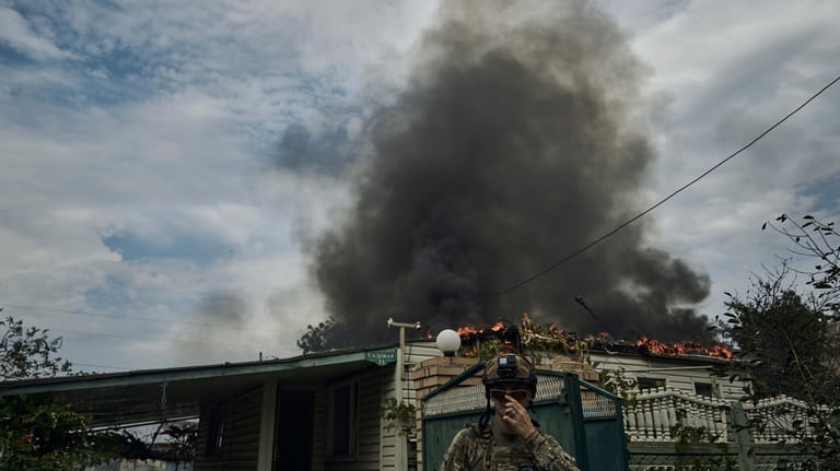 A Ukrainian soldier passes by a burning house after the...