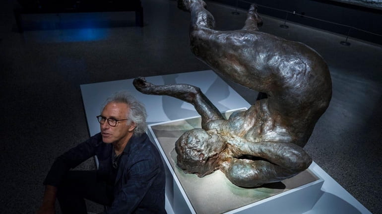Artist Eric Fischl sits next to his sculpture "Tumbling Woman"...